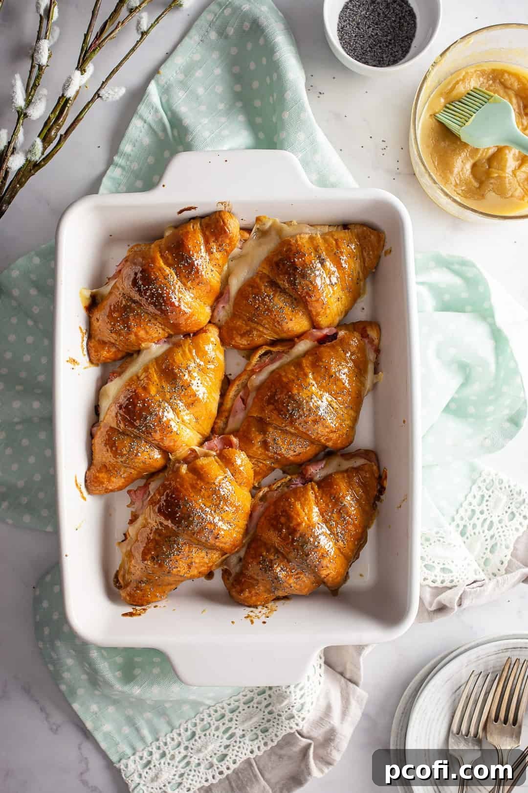A close-up of a platter of baked hot ham and cheese croissant sandwiches, showcasing their golden crusts and inviting melted cheese.