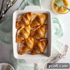 A freshly baked hot ham and cheese croissant sandwich with melted cheese peeking out, garnished with poppy seeds.