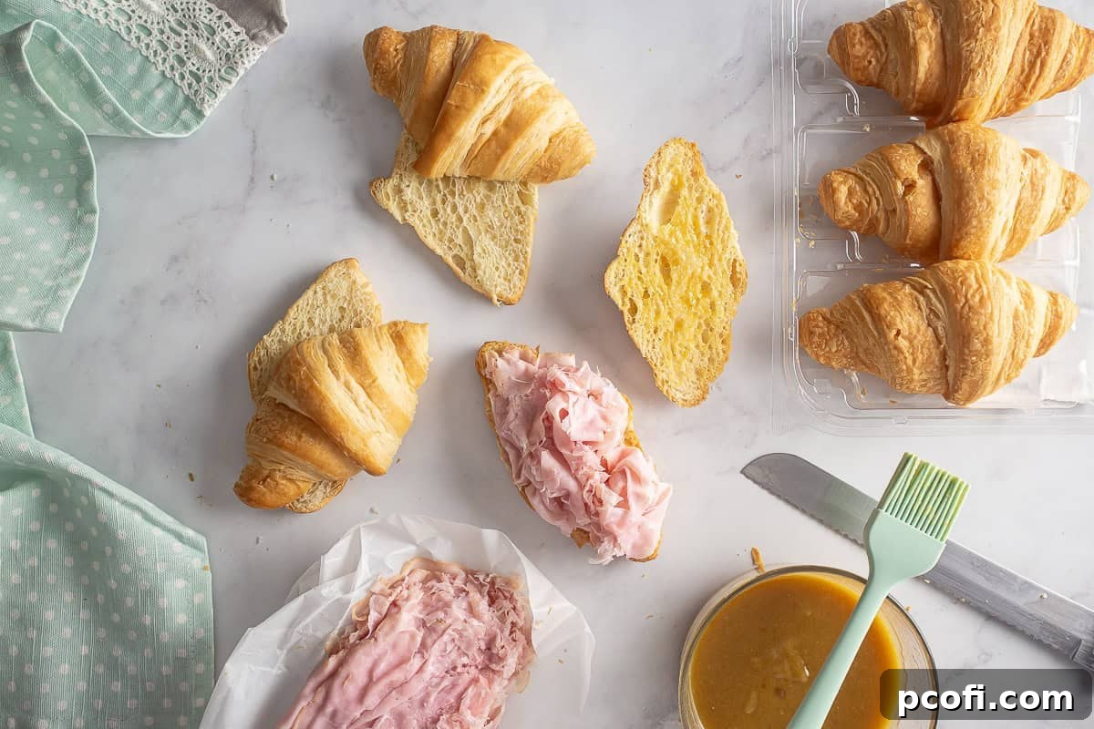 Croissants sliced horizontally with layers of thinly sliced ham placed on their bottom halves, ready for cheese.