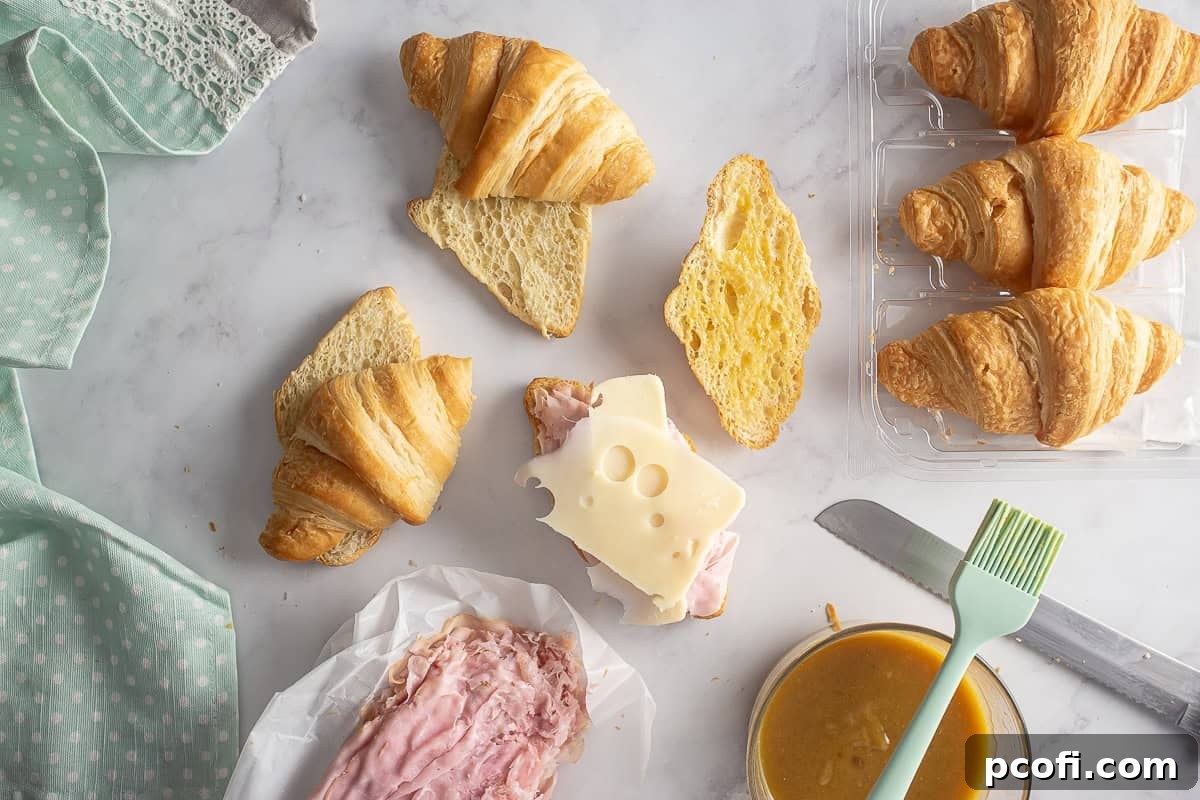 Assembled ham and cheese croissants with Swiss cheese layered over ham, before the top croissant halves are added and before baking.