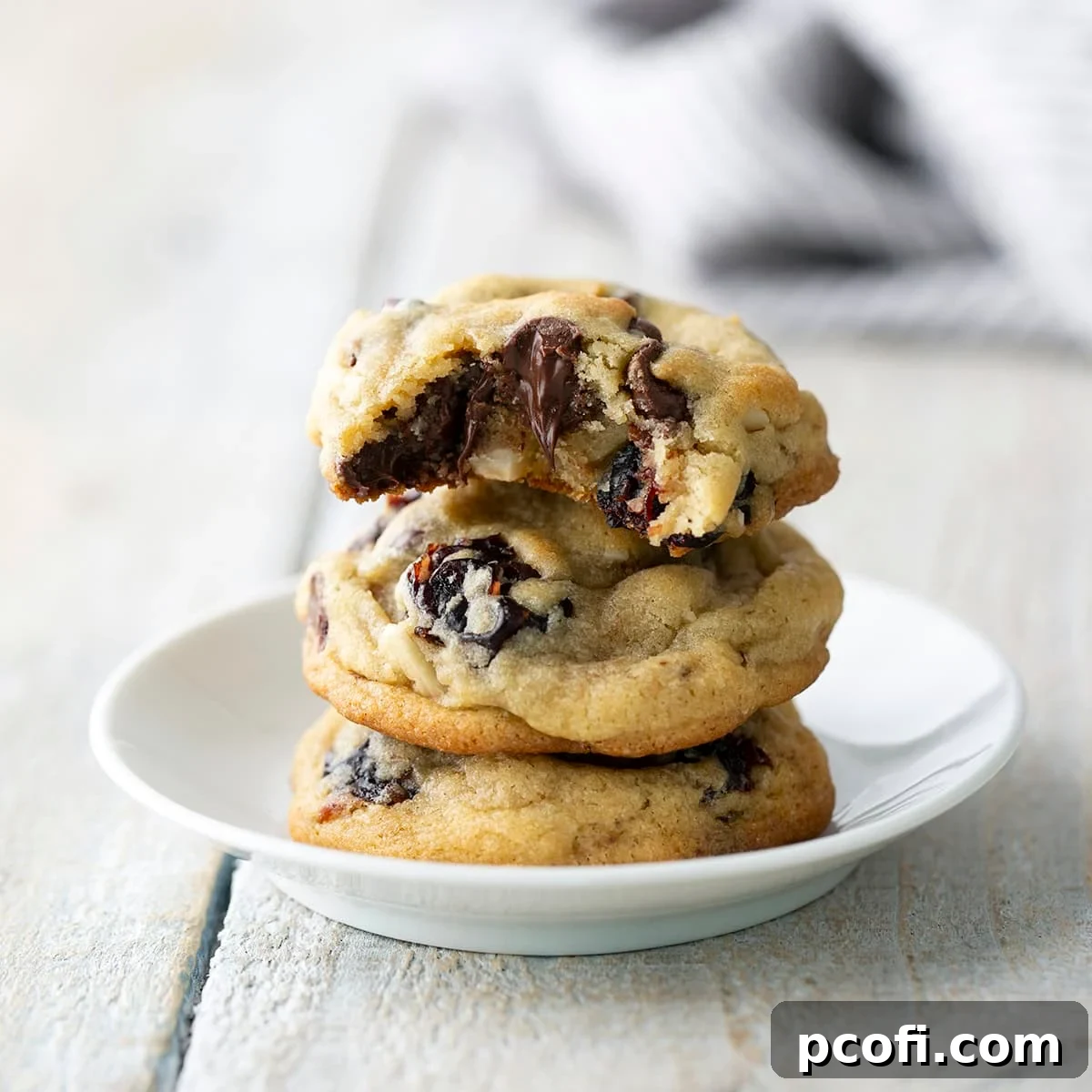 Three golden-brown cherry almond chocolate chip cookies on a white plate, showcasing their soft texture.