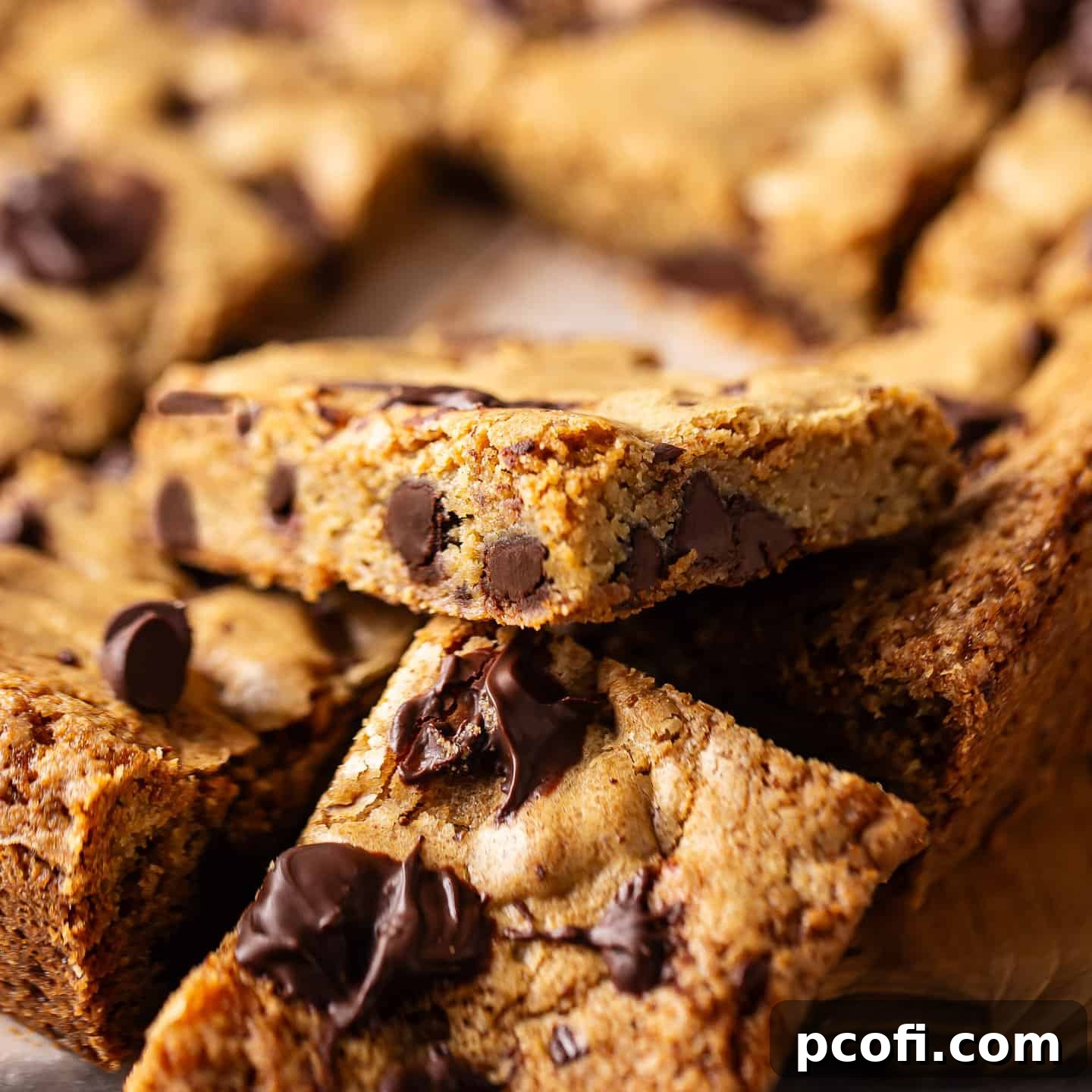 A stack of chocolate chip blondies with crinkly tops and visible melted chocolate chips.