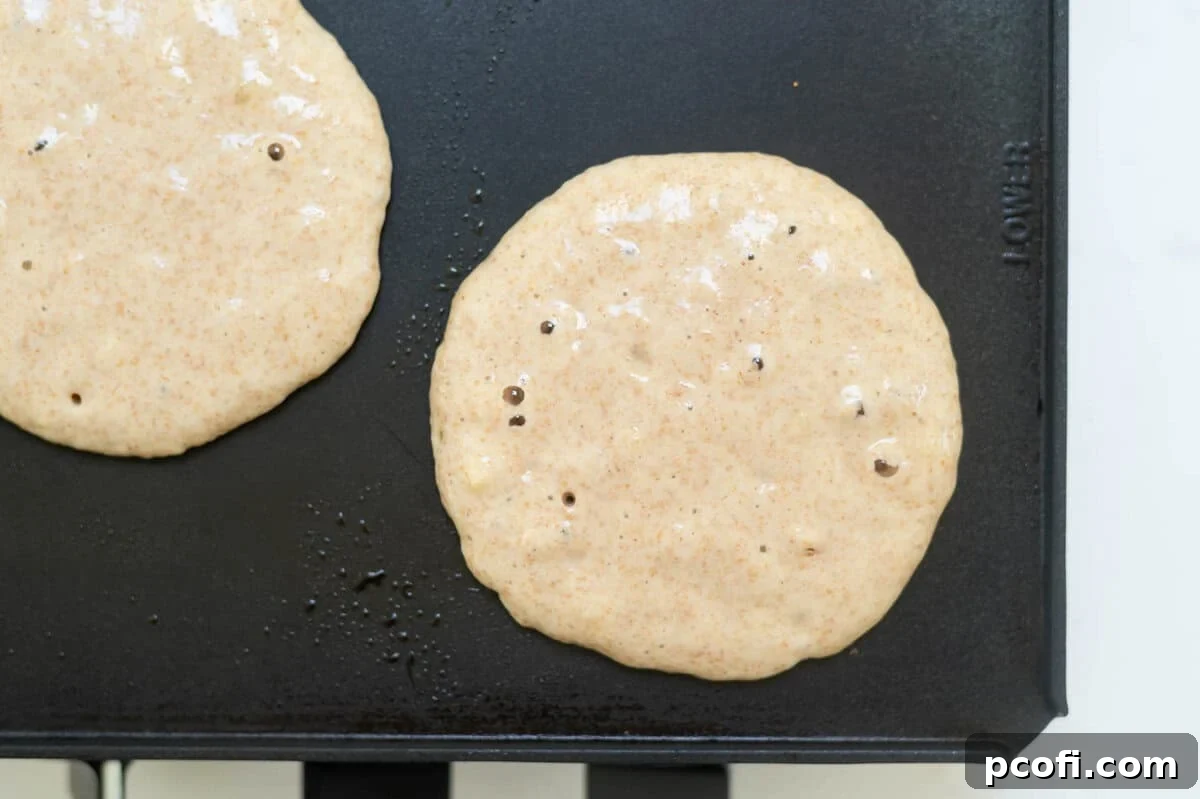 pancake batter on a griddle with large bubbles on the batter
