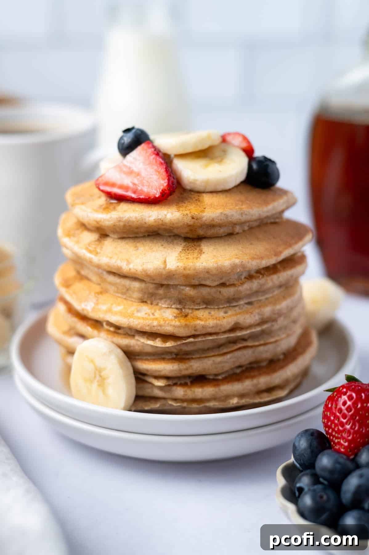 stack of pancakes with fresh fruit on top and syrup running down the sides