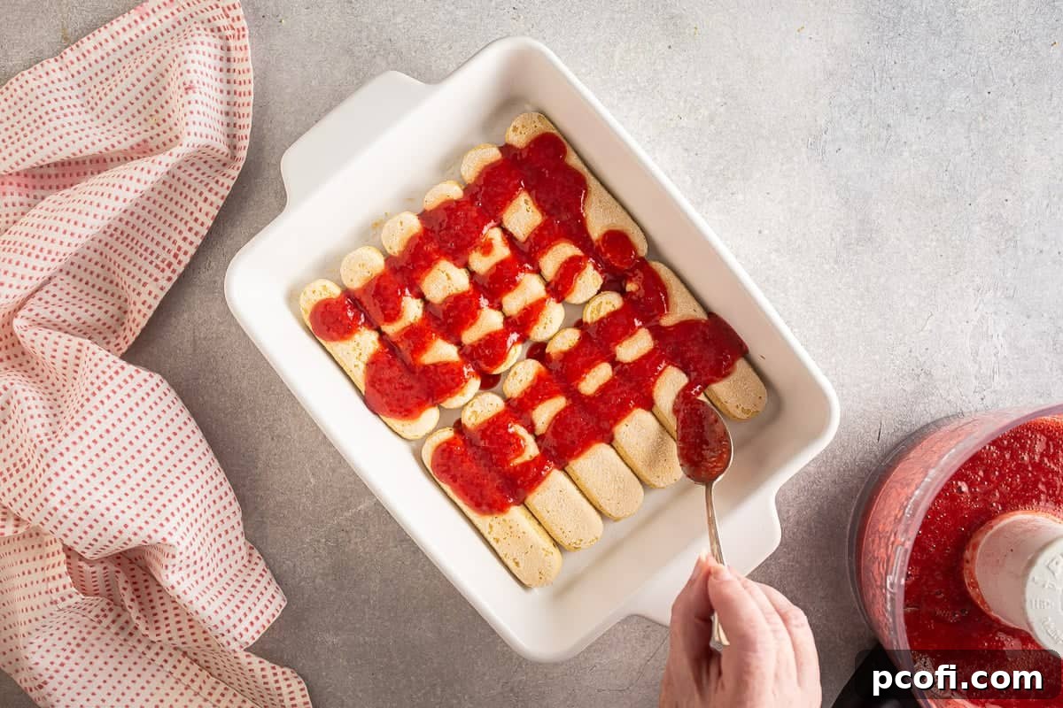 Strawberry Tiramisu Recipe with Mascarpone and Ladyfingers 13 Pouring strawberry filling over ladyfingers for strawberry tiramisu.